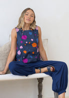 Woman sitting on a chair wearing a navy sleeveless top with colourful polka dots and navy blue pants.