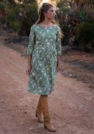 Model walks along dirt road in pale green cotton dress with boat neckline and 3/4 sleeves