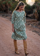 Woman wears pale green cotton over the knee length dress with 3/4 sleeves and boat neckline