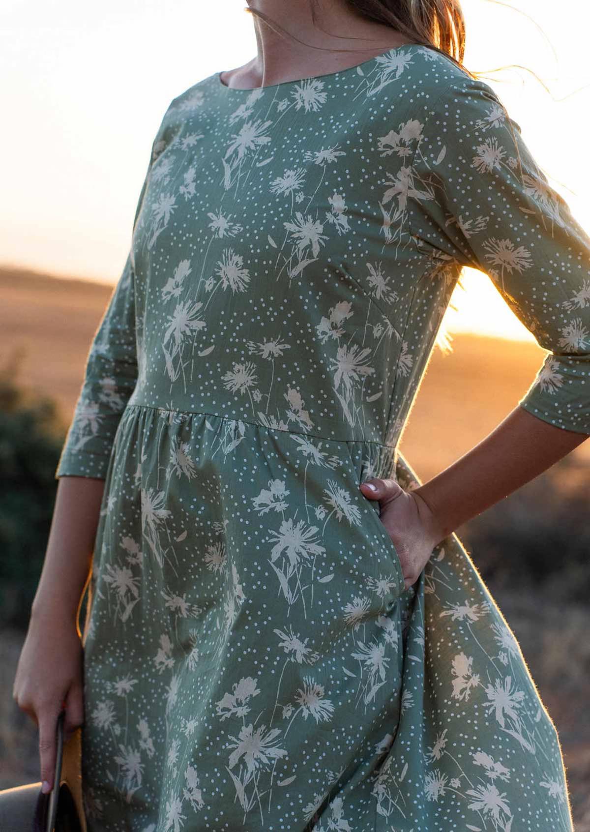 Close up of woman in cotton dress in cream floral print on pale green base with her hand in pocket