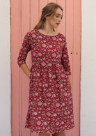 Model wears beautiful red cotton dress with wide round neckline and hand in a pocket.