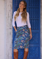 Woman wears cotton pencil skirt in leaf print on blue base with contrasting trim around the waistband and pockets