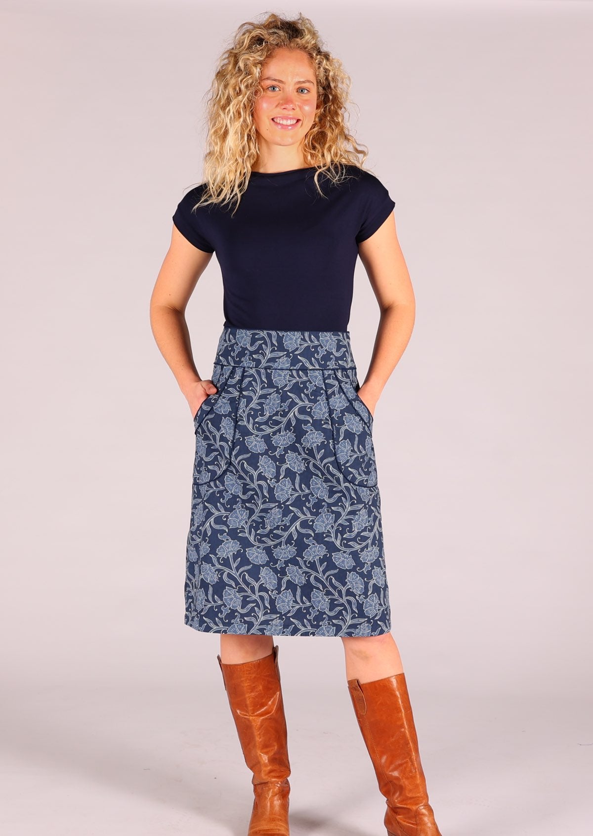 Model standing wearing Bridgette skirt Neela navy blue 100% cotton retro pencil skirt paired with a navy Wide Neck Mod top and tan leather boots