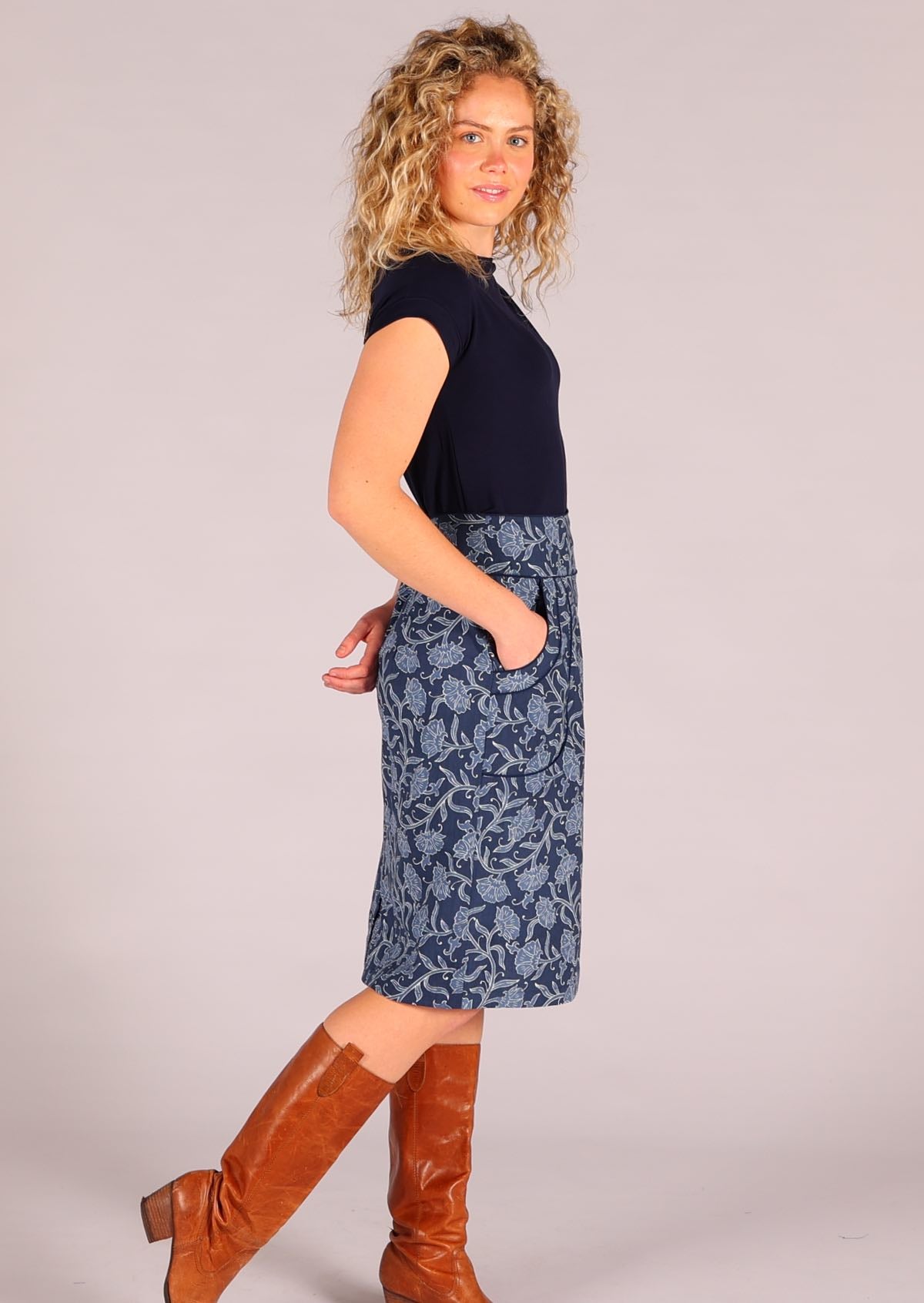 Model standing with hand in pocket wearing Bridgette skirt Neela navy blue 100% cotton retro pencil skirt paired with a navy Wide Neck Mod top and tan leather 