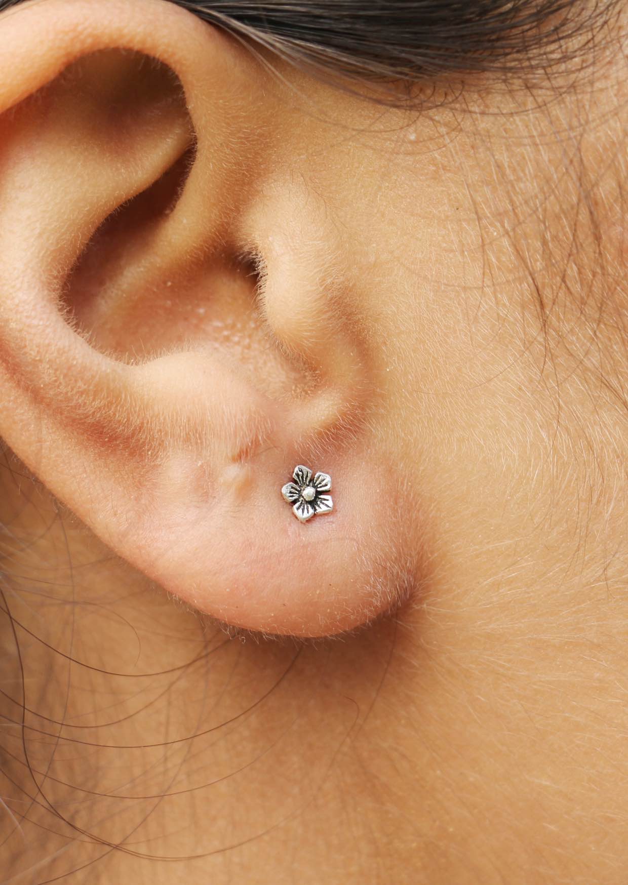 Close-up of an ear with a silver buttercup  flower-shaped studs with butterfly backs 