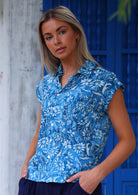 woman with blonde hair in blue cotton button up blouse in front of blue door