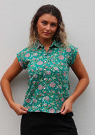 Woman wears 100% cotton cap sleeve button through shirt with collar, in jade green based floral print