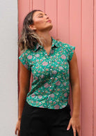 Woman wears cotton cap sleeved button through shirt with one breast pocket, in floral print on a jade green base