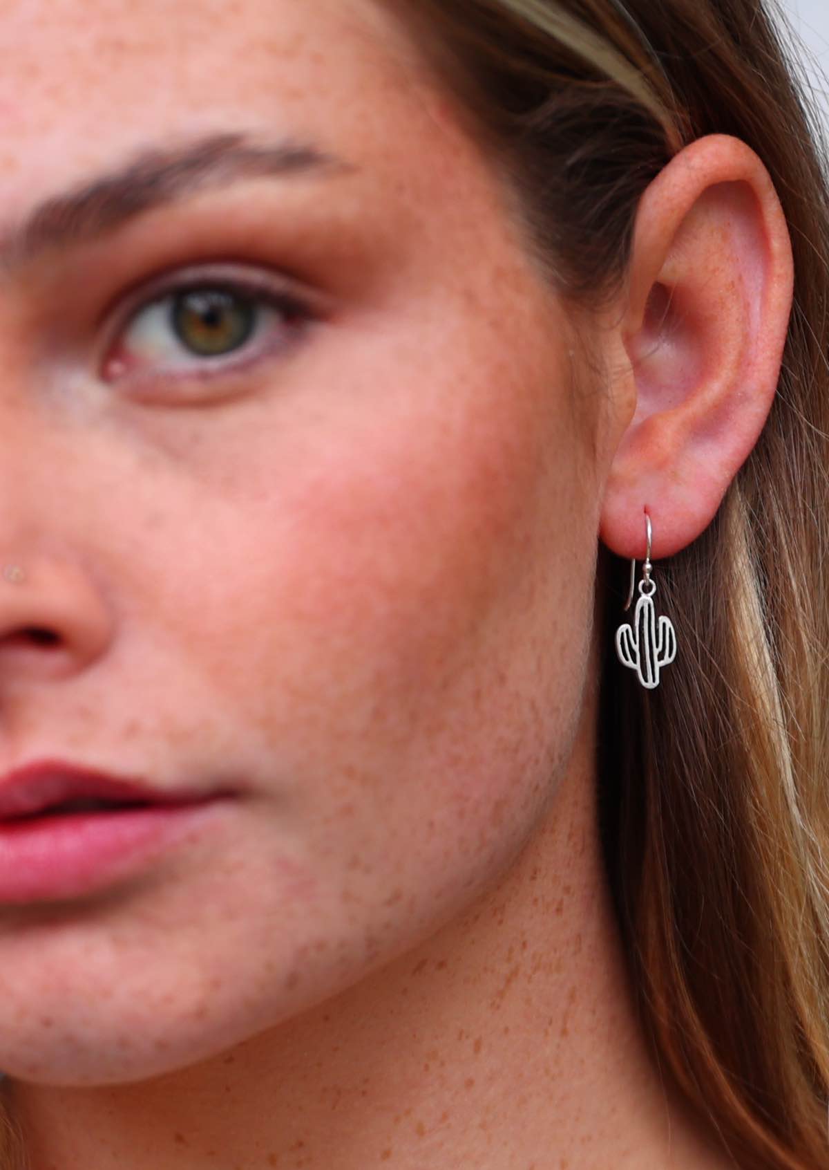 Woman wears fun sterling silver cutout cactus earrings suspended from a wire hook