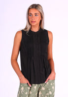 model poses in black cotton sleeveless top that sits over the hips, with a high round neckline