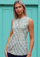 Woman wears sleeveless cotton top with yellow and green floral print on white base, with tiny pleats across chest