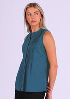 Model wears blue sleeveless cotton top that covers the hips, with tiny pleats across bust that make the lower half a relaxed fit