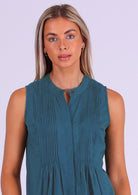 Close up of woman in blue cotton sleeveless top with high round neckline and decorative pleats