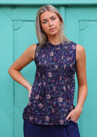 Woman poses in cotton sleeveless top that sits over the hips, in a floral print with a dark base