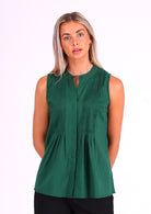 Woman in dark green sleeveless cotton top that buttons through the front with hidden button and one visible at the front of the neckline