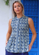 Woman stands in a cotton sleeveless top with tiny pleat detail across the bust that flares slightly below the waist