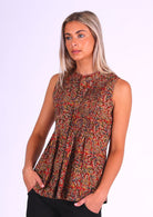 Woman in cotton sleeveless top with high round neckline and decorative pleats, in Indian floral print in warm colours