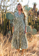 Woman stands in cotton tiered maxi dress with buttoned bodice forming a V-neckline and mandarin collar