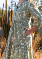 Close up of cotton maxi dress in pale green based cream floral print with models hand in pocket