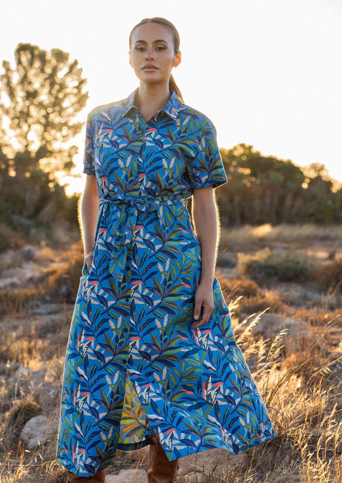 Model wears cotton shirt dress with collar, short sleeves and thick waist tie, in blue based leafy print