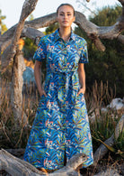 Model poses in cotton shirt dress with short sleeves and thick waist tie in leafy print on a blue base