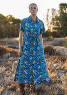 Woman poses in cotton long button through shirt dress with collar and thick waist tie