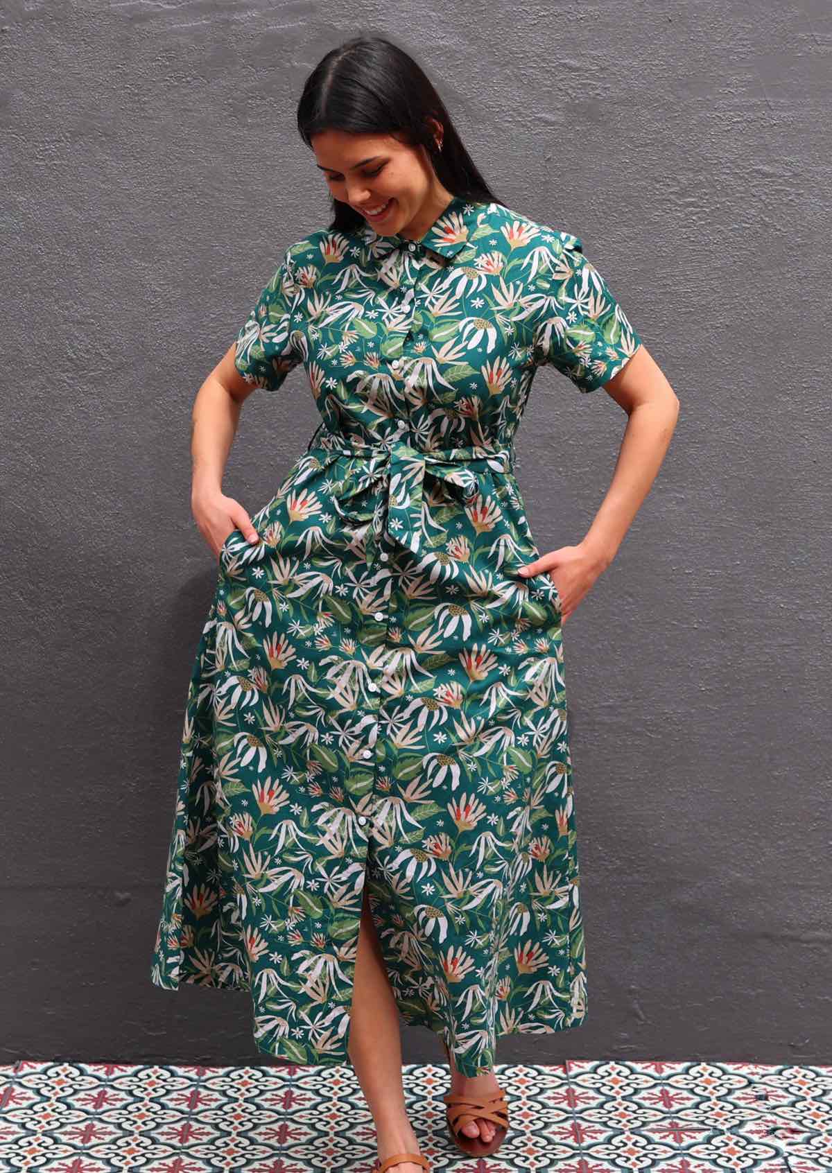 Woman with dark hair wearing 100% cotton green floral shirt dress, buttons up front, hands in pockets