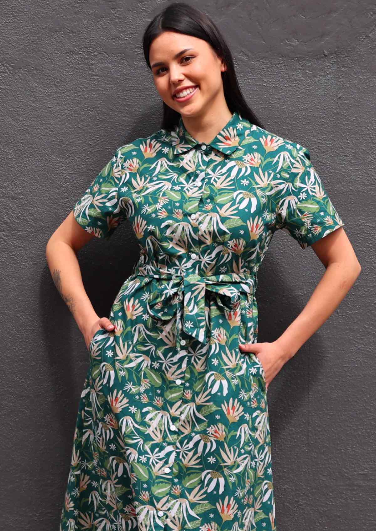 Woman with dark hair wearing 100% cotton green floral shirt dress, buttons up front and collar