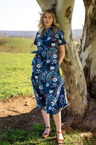 Model wearing Chelsea Dress Gardenia blue base print dress 100 percent cotton shirt dress featuring pockets, waist tie, and collar