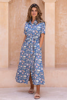 Model stands in a short sleeve, button through cotton dress with collar, detachable waist tie and pockets.