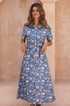 Woman wearing a blue floral button through shirt dress standing against a beige wall.