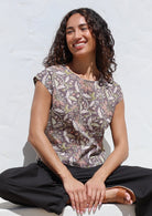 Woman sitting on a white surface wearing printed cap sleeved cotton top in grey with delicate beige, pink and lime floral print 