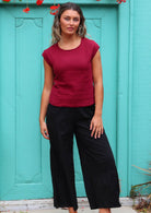 Woman stands in deep red double cotton simple top with cap sleeves paired with black cotton pants