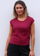 Woman wears cotton gauze top with round neckline and cap sleeves in deep red colour