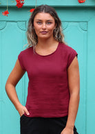 Woman wears cotton cap sleeve top with round neckline in deep red colour with her hand in pocket of pants