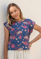 Woman stands in cotton cap sleeved top with high round neckline, in blue based pink, burgundy and grey floral print 