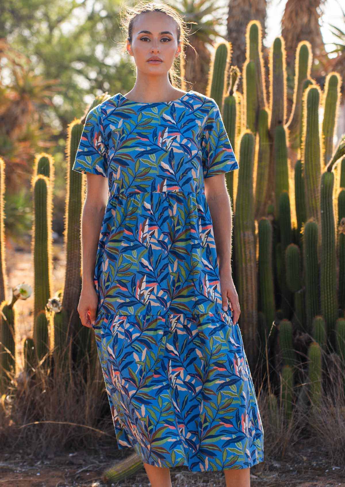 Model poses in cotton midi length short sleeve dress with leafy print on a blue base