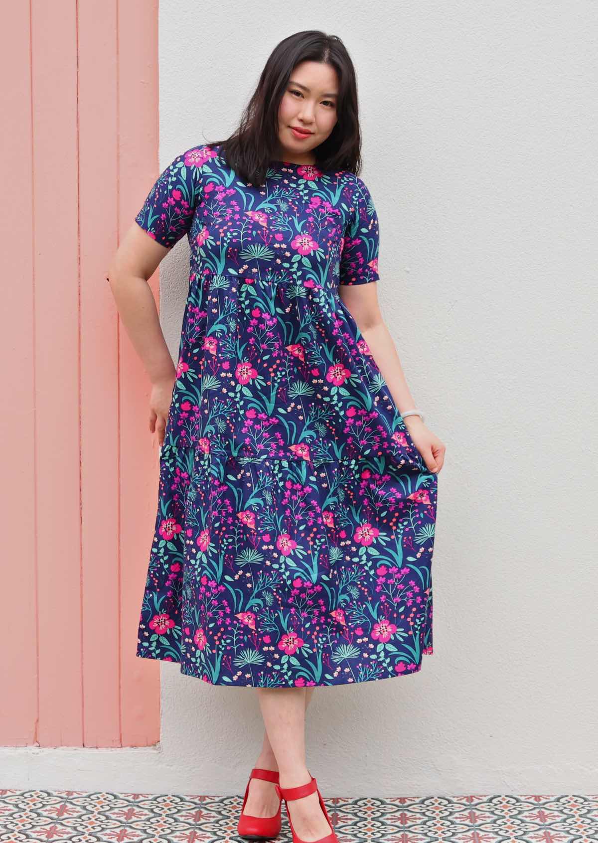 Model wearing shin length pink and purple floral on dark blue base 100 percent cotton sundress 