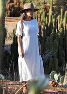 woman wearing white pure cotton maxi dress with hat in front of cacti 