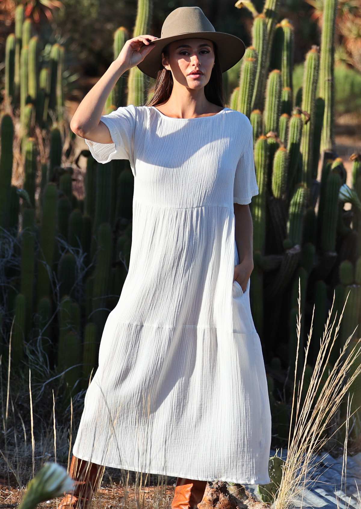 woman wearing white cotton maxi dress with hat in front of cacti 