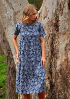 Model standing by a tree wearing Claudia Dress Neela navy blue 100 percent cotton maxi sundress