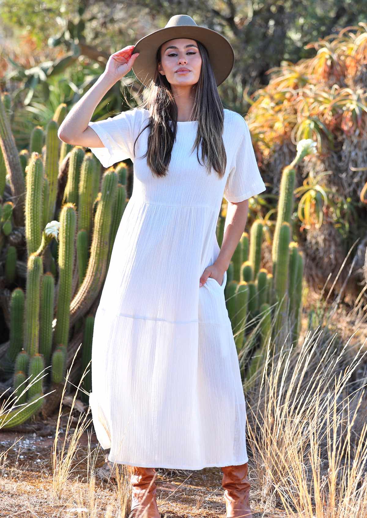 Woman with dark hair in beautiful 
white cotton maxi dress with hands in pockets 