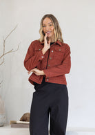 Woman wearing a rust-colored jacket and black pants against a white background
