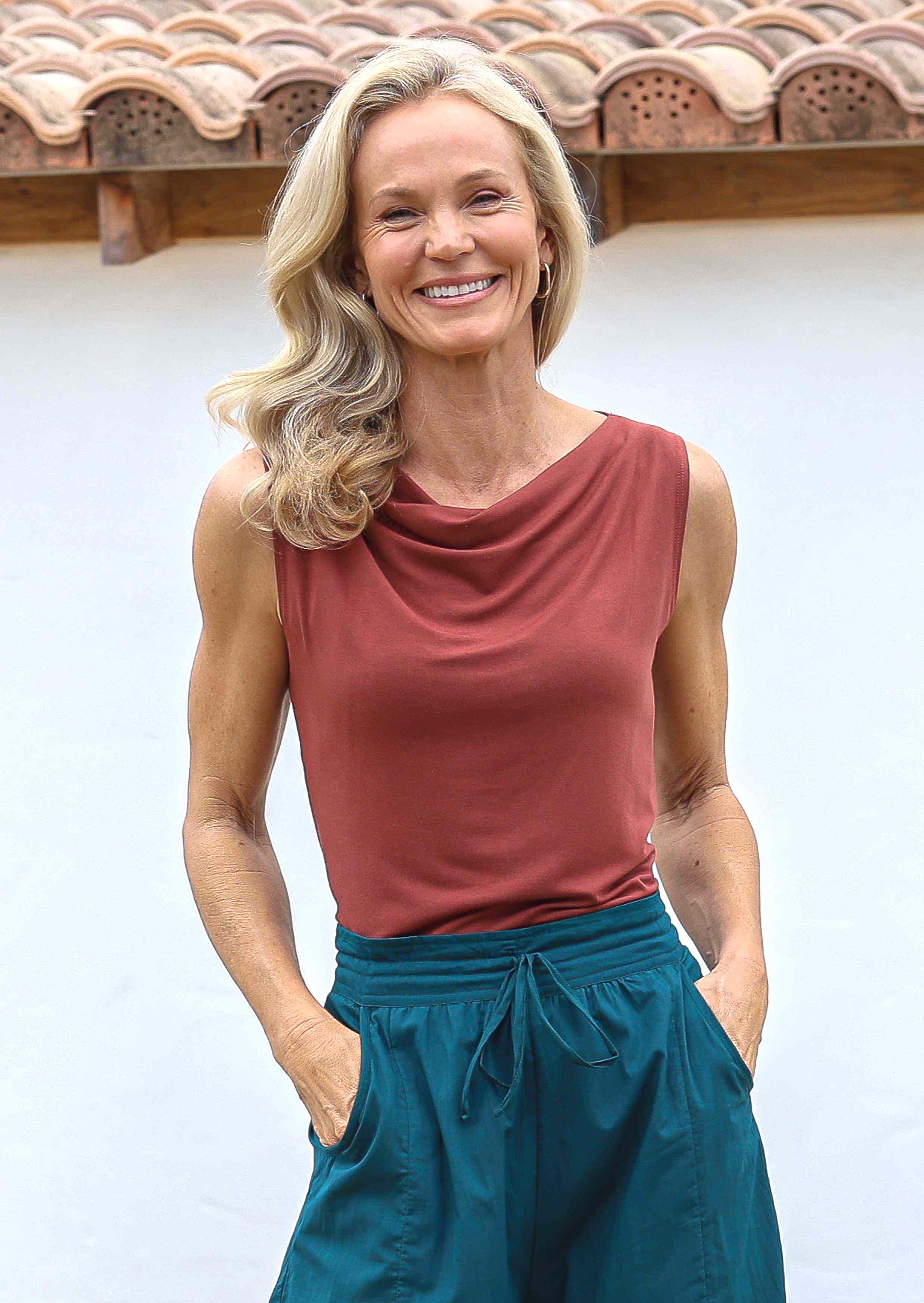 Woman wearing a terracotta coloured sleeveless top with a cowl neckline and teal pants