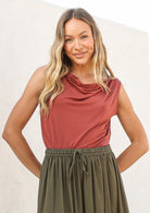 Woman wearing a terracotta coloured sleeveless top with a cowl neckline, tucked into olive green skirt