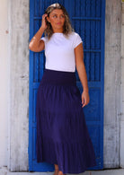 Woman wearing navy blue cotton maxi skirt with white t-shirt in front of bright blue door