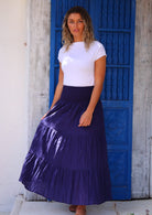 Woman wearing navy blue cotton maxi skirt with elastic waist, flared skirt and white t-shirt in front of bright blue door