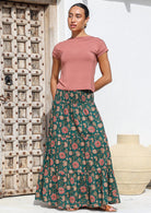 Woman stands in deep green floral print cotton maxi skirt with a wide shirred elastic waistband paired with a dusty rose stretch rayon top.