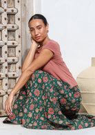 Model seated gracefully wearing a tiered cotton maxi skirt in green based floral print.