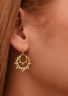 Close-up of a woman wearing delicate gold coloured crescent hoop earrings that have open cut-out detailing and mini bead accents.